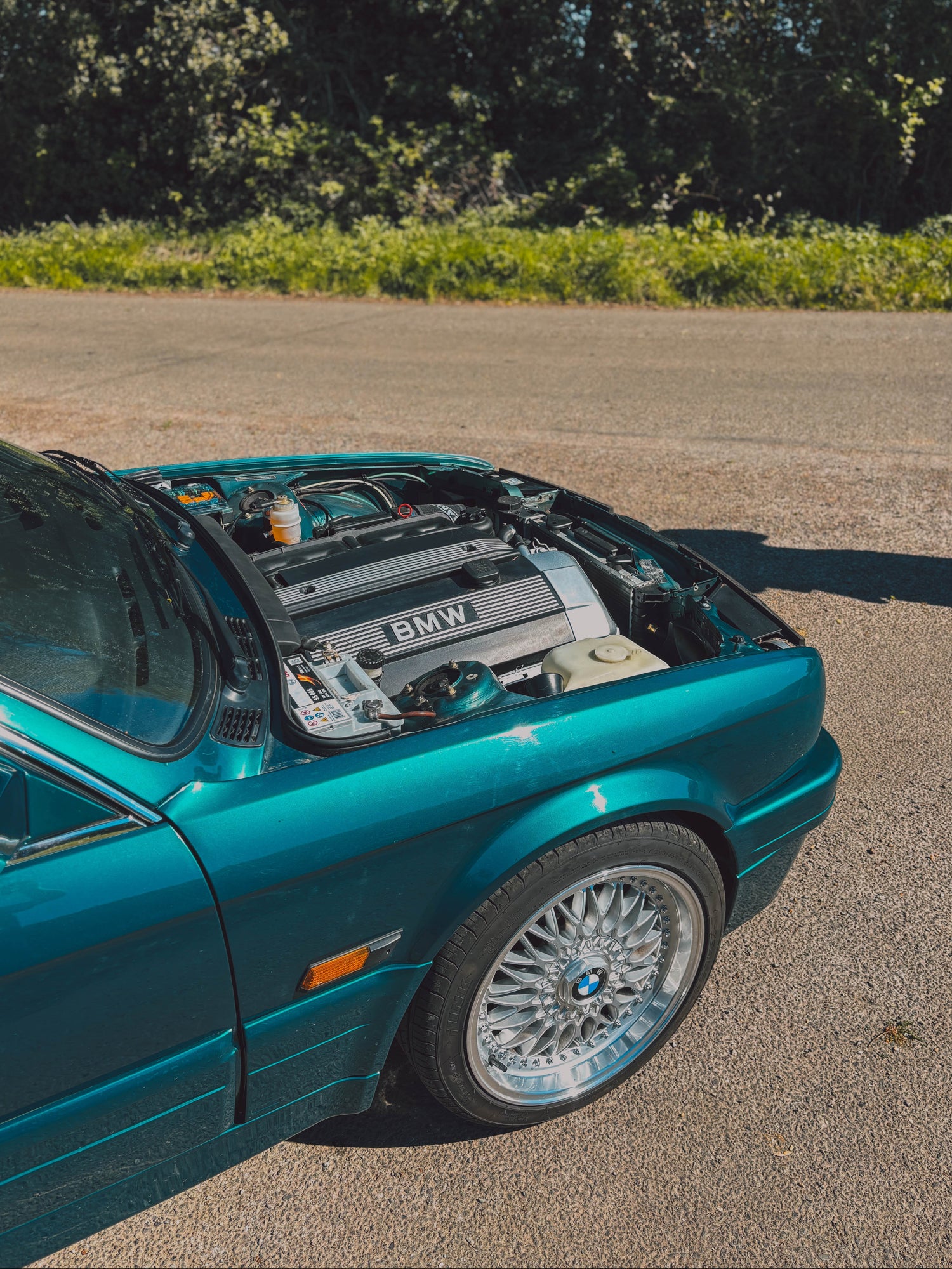 A teal BMW E30 with its bonnet open, showing the engine bay, and its swapped M54 engine