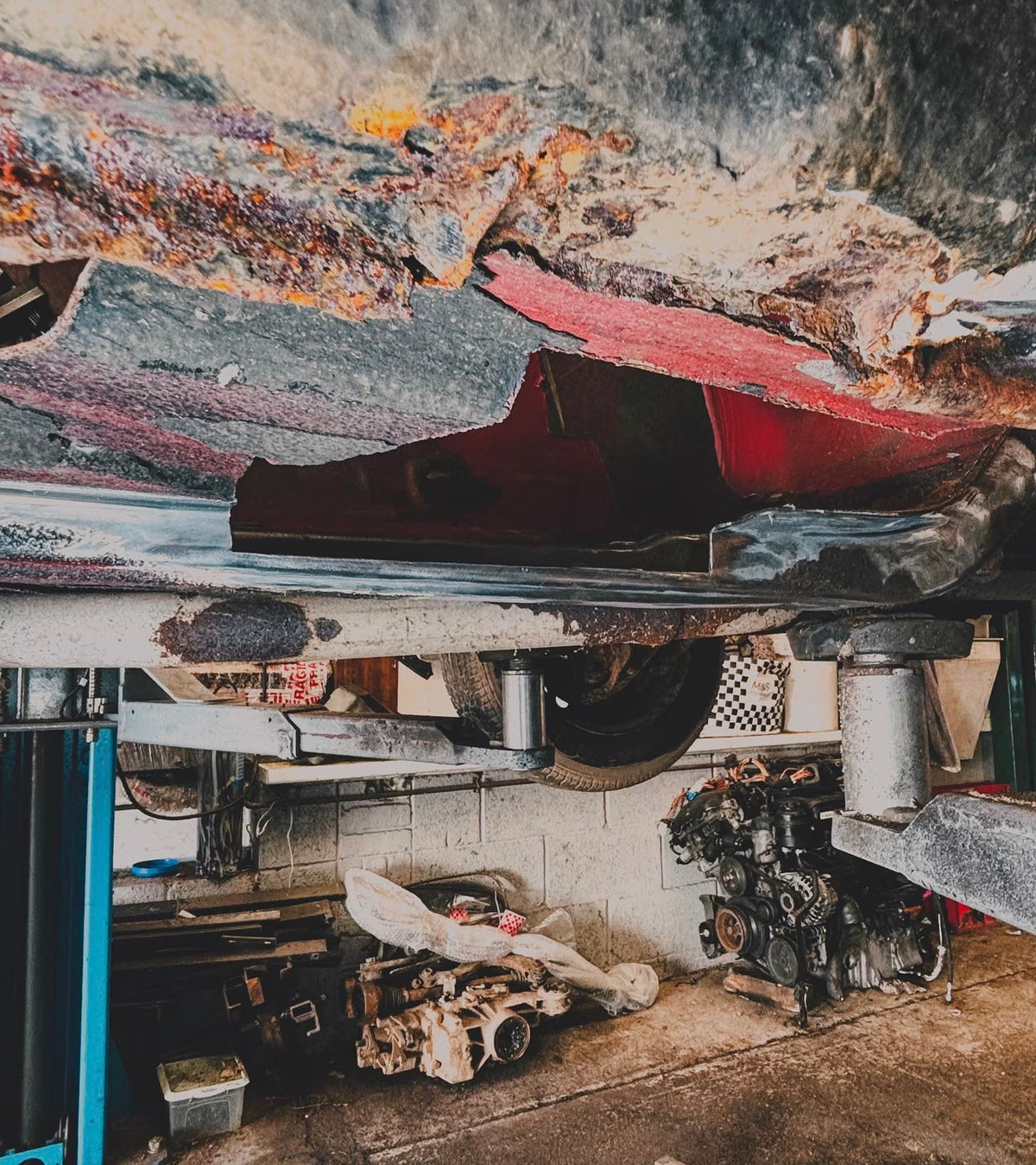 A BMW E30 in a car workshop on a lift showing extensive rust on the sills.